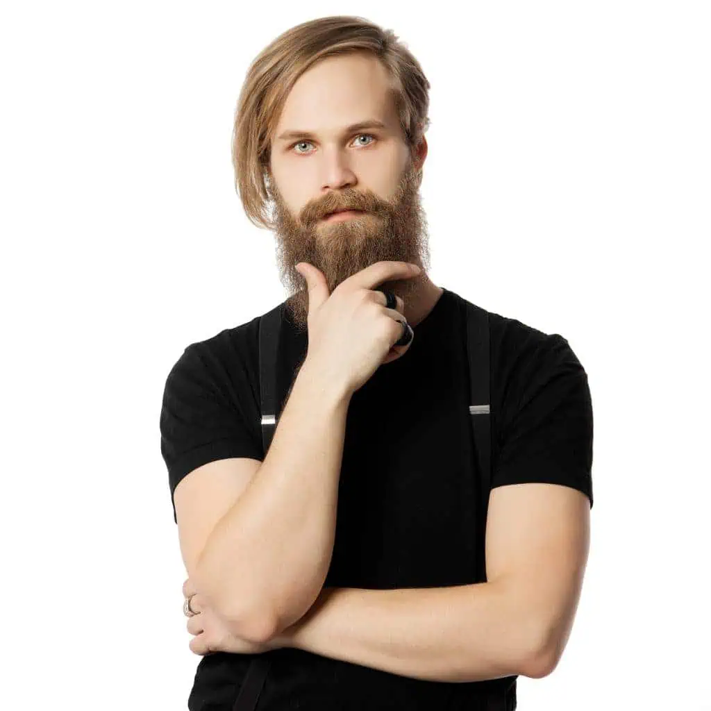 the thoughtful attractive man the blonde with long hair of the European appearance with a beard with braces keeps a hand at a chin on a white background in a black t-shirt